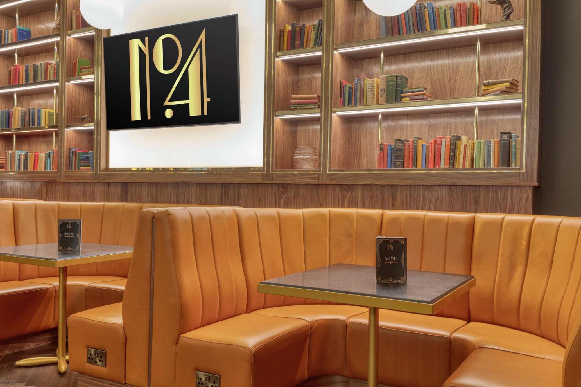 Hilton Belfast Hotel Exterior photo The photo shows a cozy interior space featuring a stylish seating area. There are plush, orange leather booths with an elegant design, arranged around small tables. The background includes a wooden bookshelf filled with a variety of colorful books. A