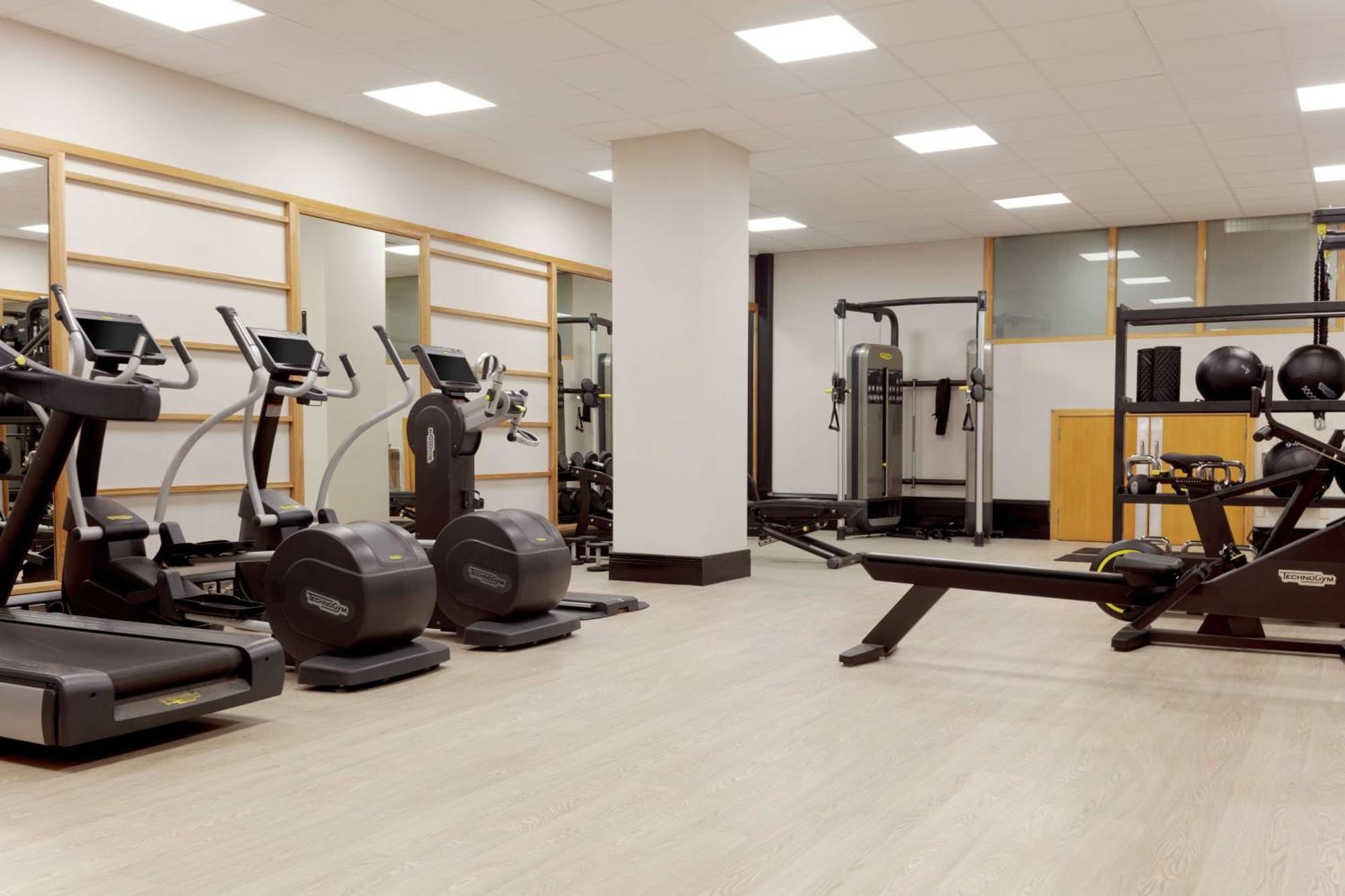 Hilton Belfast Hotel Exterior photo The photo shows a gym or fitness area. It features several exercise machines, including treadmills and elliptical machines. There's also a rowing machine and a multi-station strength training equipment. The space is well-lit with overhead lights and 
